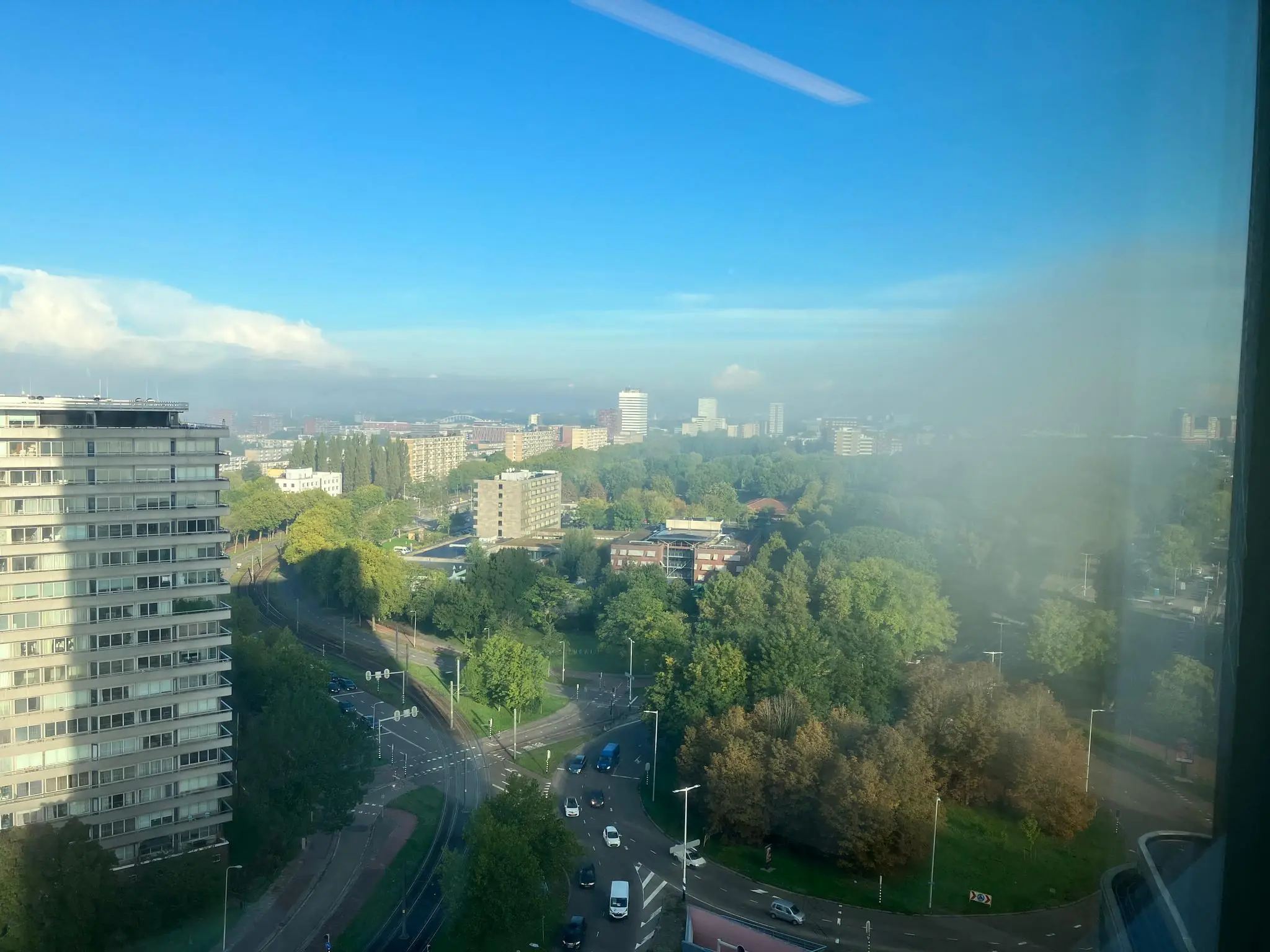Uitzicht op de Vliegend Hertlaan in Utrecht met gebouwen, bomen en een rotonde onder een heldere blauwe hemel.